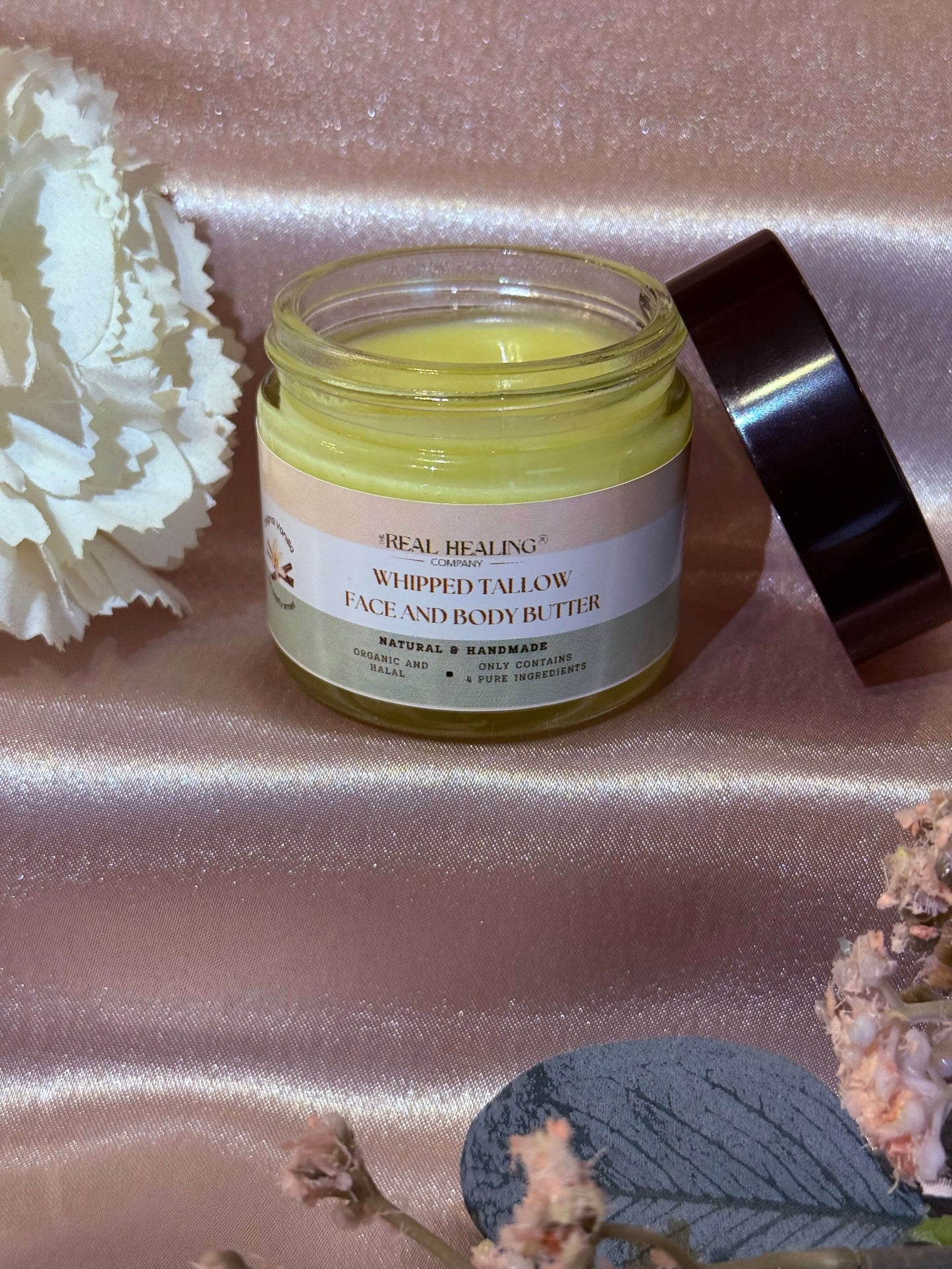 Whipped Tallow Face and Body Butter in a glass jar on a satin background, showcasing its luxurious texture.