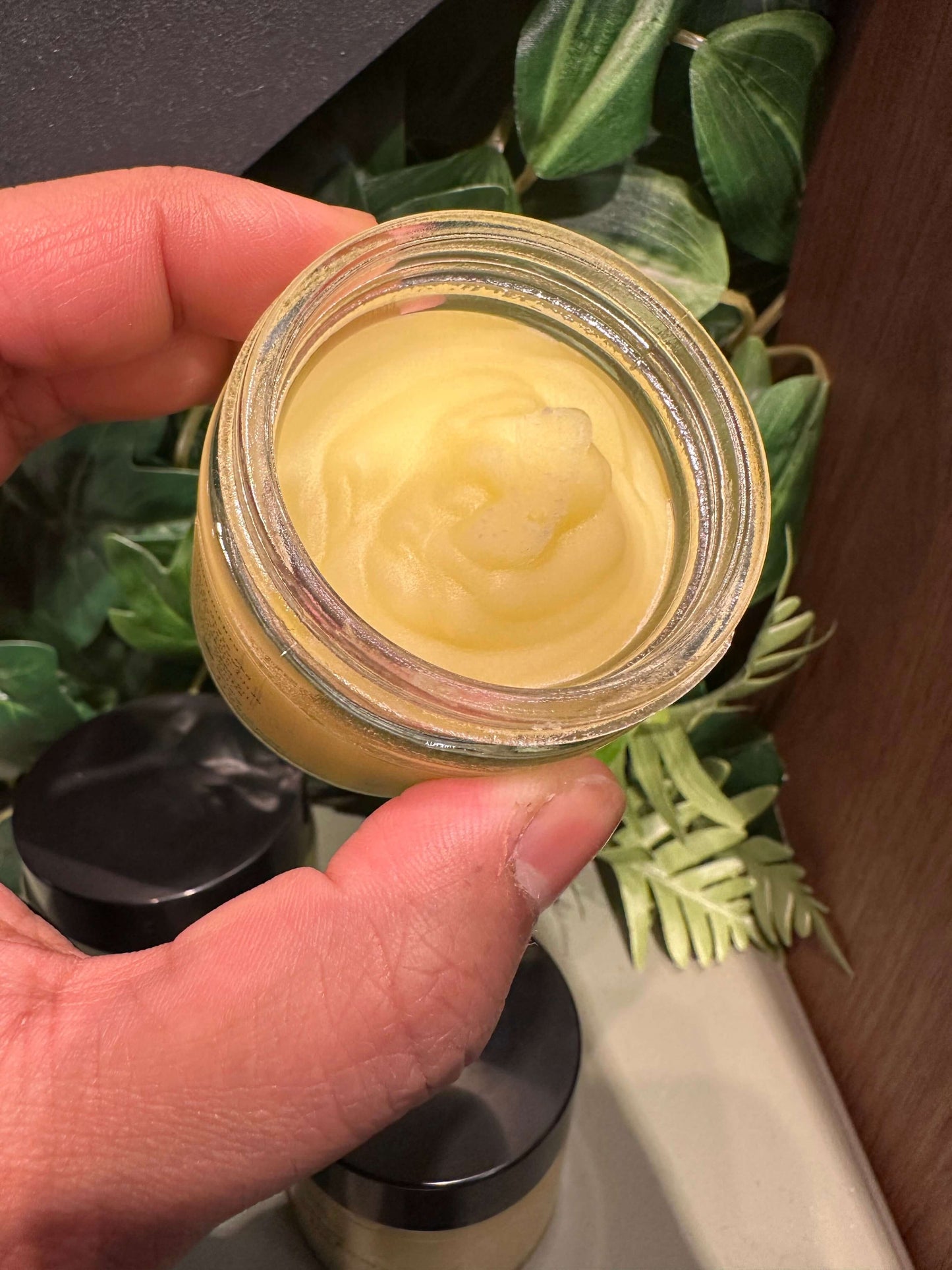 Hand holding a jar of whipped tallow face and body butter with a smooth, creamy texture.