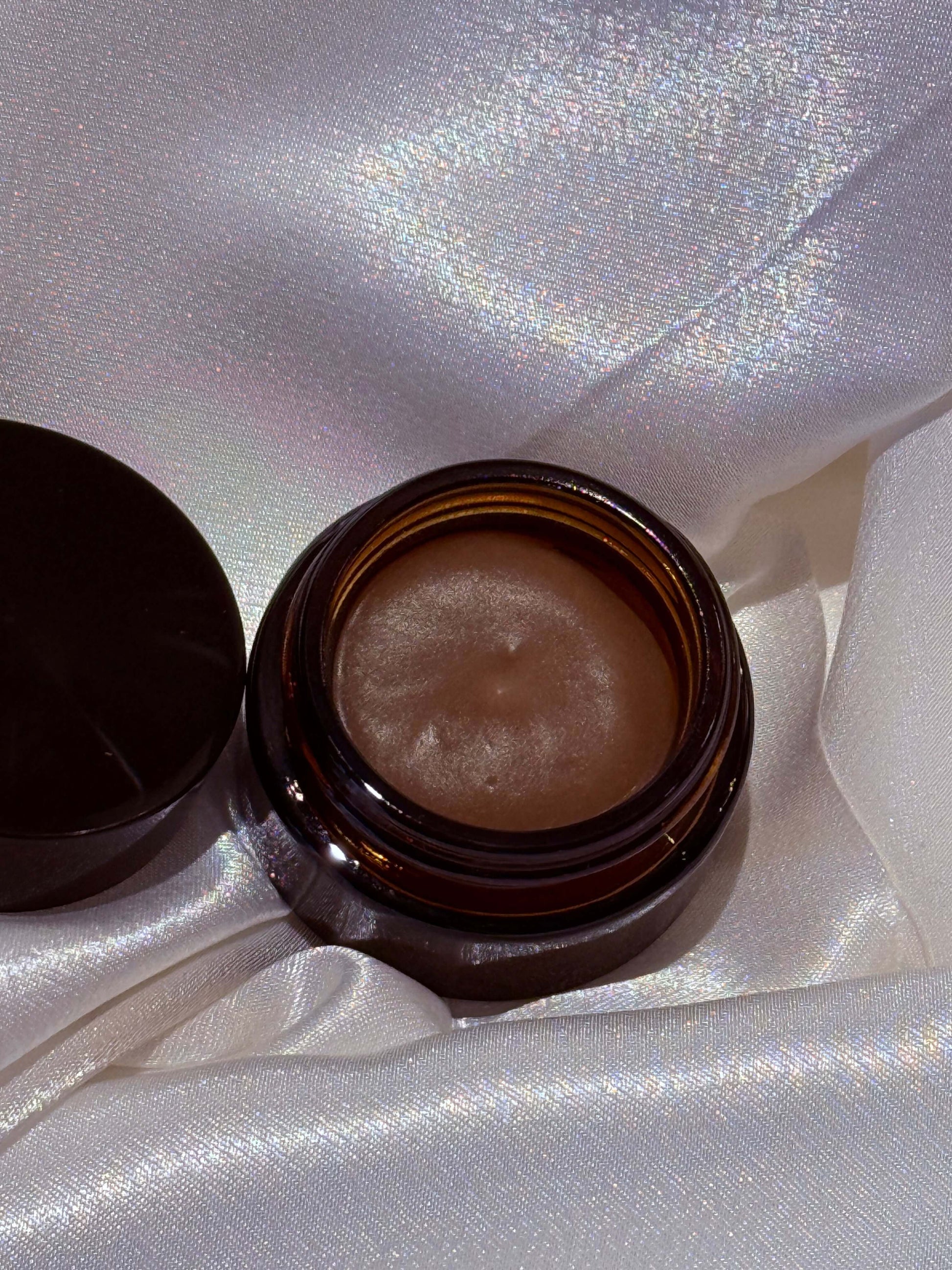 Espresso Eyes coffee infused tallow eye cream in amber jar resting on silky fabric.